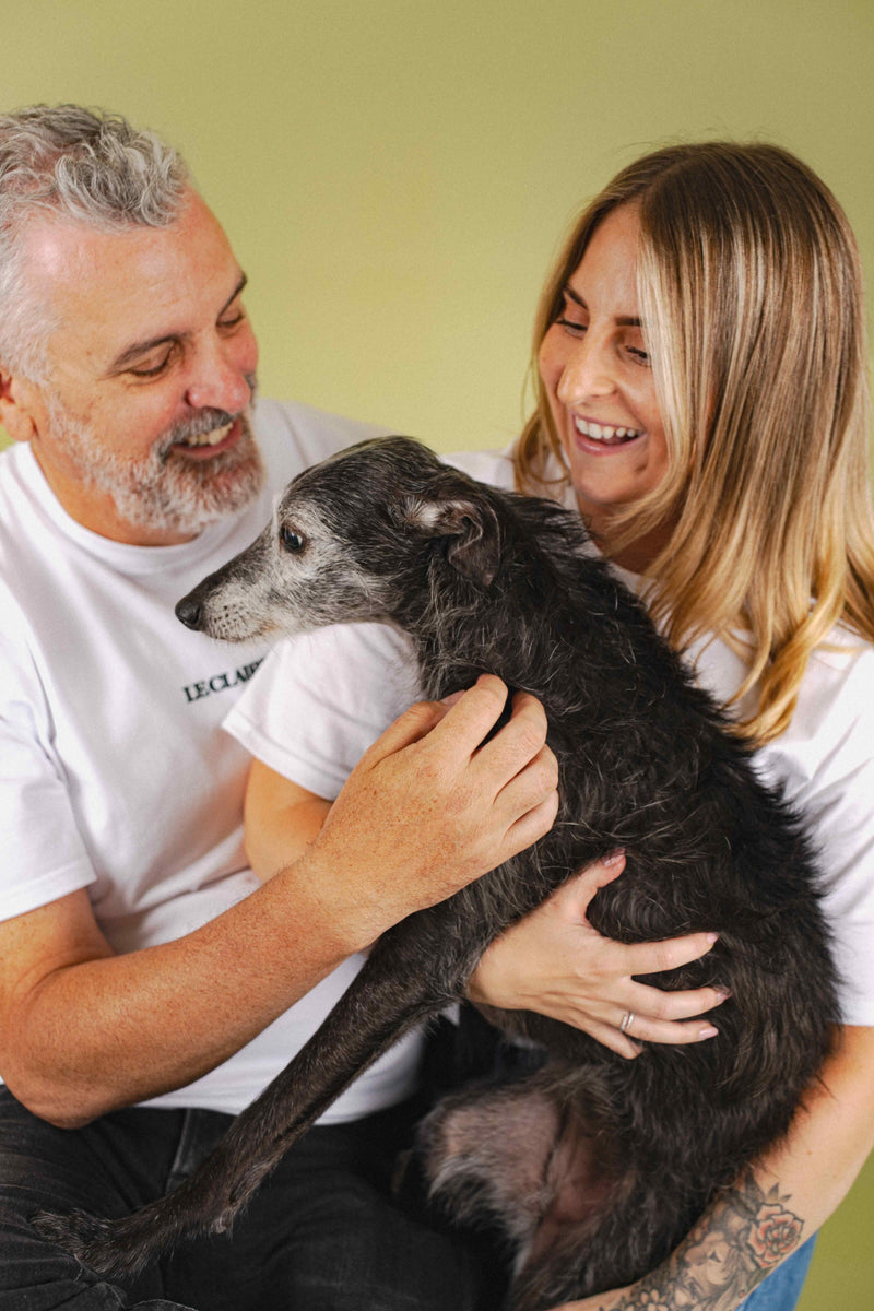 Man and woman holding a dog against a green background
