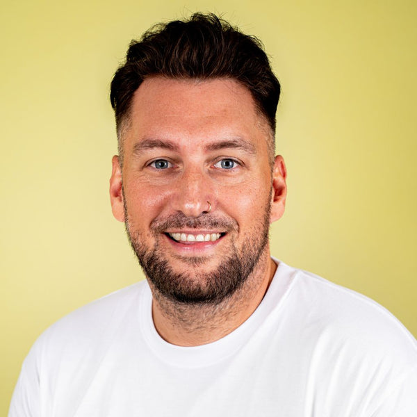 Man with a beard wearing a white shirt against a yellow background