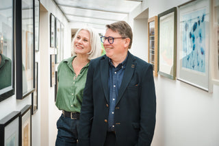 Two people standing in a room with framed artwork on the walls.