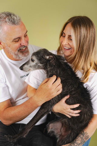 Man and woman holding a dog against a green background
