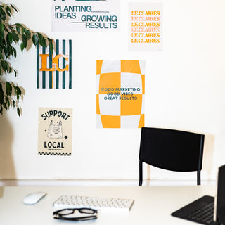 A styled office workspace featuring a collection of colorful graphic art prints on a white wall above a desk with a keyboard, mouse, and chair.